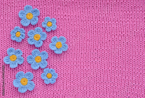 Handmade blue crocheted flowers on a pink knitted background.
