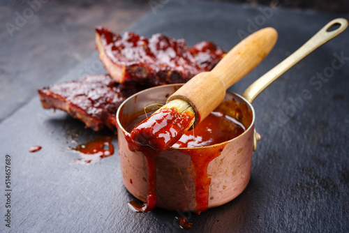 Canvas Print Hot and spicy barbecue sauce in a casserole as close-up with spare ribs in backg