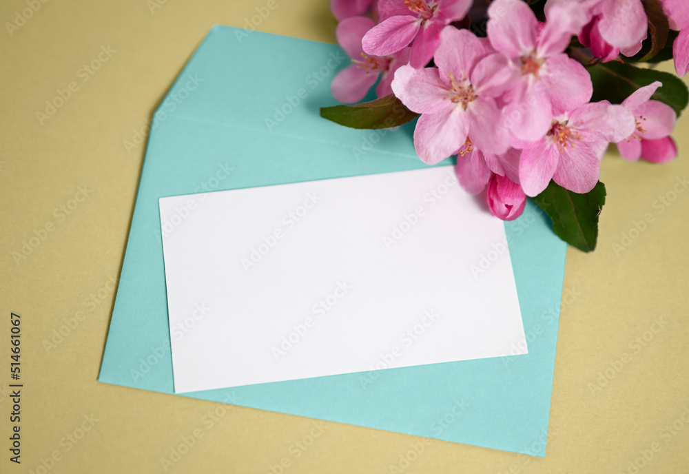 Spring composition. Mockup with envelope and blank card. Turquoise envelope on a yellow background and blossoming branch of an apple tree. Spring composition. Mockup with envelope and blank card. Turquoise envelope on a yellow background and blossoming branch of an apple tree.