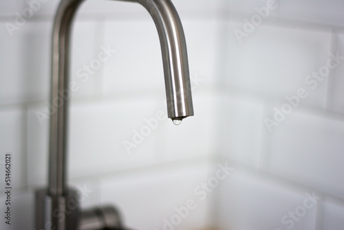 Water drips from the tap on the background of white tiles in the kitchen