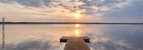 Busnieku lake at sunset. Ventspils, Latvia. Wooden pier. Soft sunlight, glowing clouds, symmetry reflections in a crystal clear water. Spring, early summer. Panoramic view. Nature, ecology, ecotourism photo