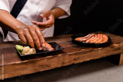 Chef's hand holding fresh piece of salmon.Closeup of chef hands preparing japanese food. Japanese chef making sushi at restaurant.Chef making traditional japanese sushi on wood board.