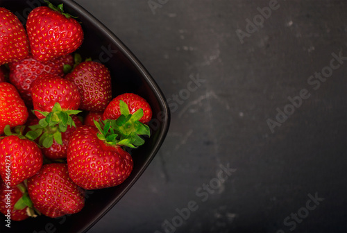 A bowl of fresh, juicy strawberries against a dark, stony background. Top view. Space for text