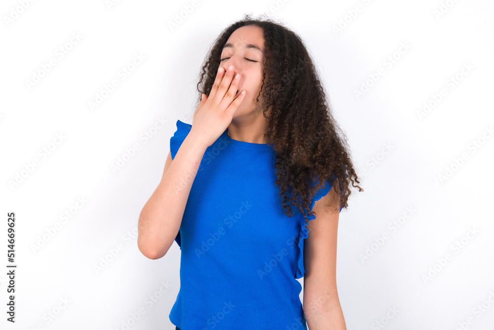 Teenager girl with afro hairstyle wearing blue T-shirt over white wall being tired and yawning after spending all day at work. Teenager girl with afro hairstyle wearing blue T-shirt over white wall being tired and yawning after spending all day at work.