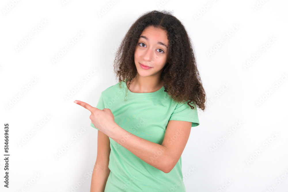 Teenager girl with afro hairstyle wearing green T-shirt over white wall Pointing aside worried and nervous with forefinger, concern and surprise concept. Teenager girl with afro hairstyle wearing green T-shirt over white wall Pointing aside worried and nervous with forefinger, concern and surprise concept.