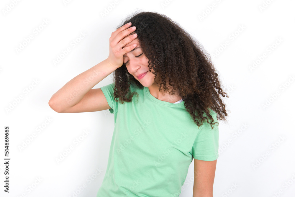 A very upset and lonely Teenager girl with afro hairstyle wearing green T-shirt over white wall crying, A very upset and lonely Teenager girl with afro hairstyle wearing green T-shirt over white wall crying,