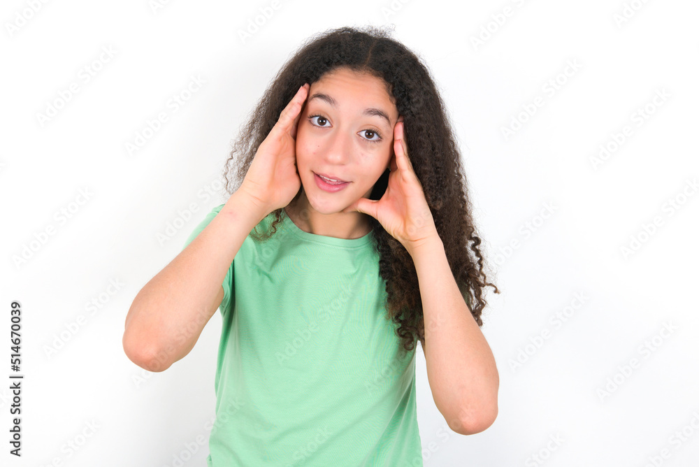 Teenager girl with afro hairstyle wearing green T-shirt over white wall Pleasant looking cheerful, Happy reaction Teenager girl with afro hairstyle wearing green T-shirt over white wall Pleasant looking cheerful, Happy reaction