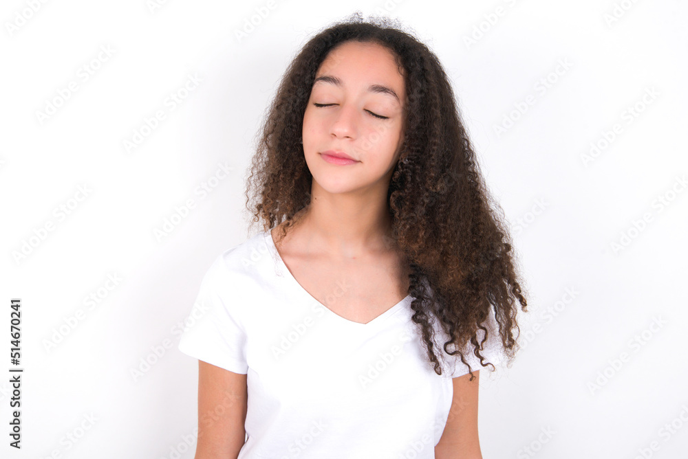 Teenager girl with afro hairstyle wearing white T-shirt over white wall nice-looking sweet charming cute attractive lovely winsome sweet peaceful closed eyes Teenager girl with afro hairstyle wearing white T-shirt over white wall nice-looking sweet charming cute attractive lovely winsome sweet peaceful closed eyes