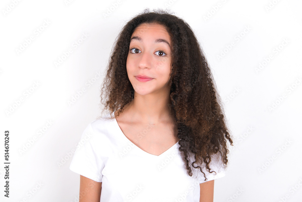 Stunned Teenager girl with afro hairstyle wearing white T-shirt over white wall stares reacts on shocking news. Astonished teen girl holds breath Stunned Teenager girl with afro hairstyle wearing white T-shirt over white wall stares reacts on shocking news. Astonished teen girl holds breath