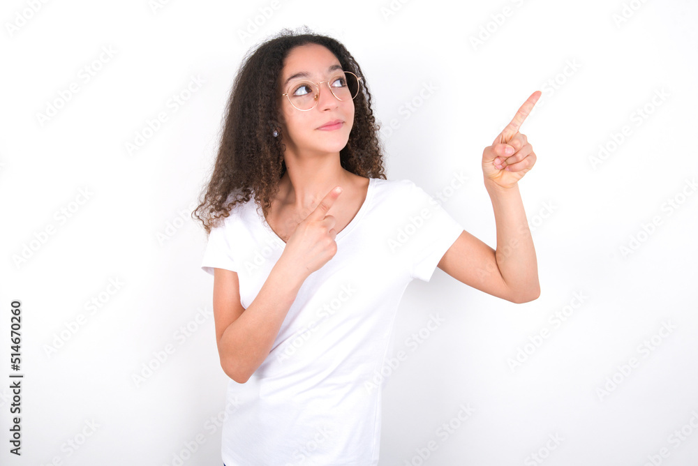Teenager girl with afro hairstyle wearing white T-shirt over white wall smile excited directing fingers look empty space Teenager girl with afro hairstyle wearing white T-shirt over white wall smile excited directing fingers look empty space
