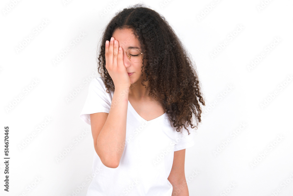Teenager girl with afro hairstyle wearing white T-shirt over white wall with sad expression covering face with hands while crying. Depression concept. Teenager girl with afro hairstyle wearing white T-shirt over white wall with sad expression covering face with hands while crying. Depression concept.