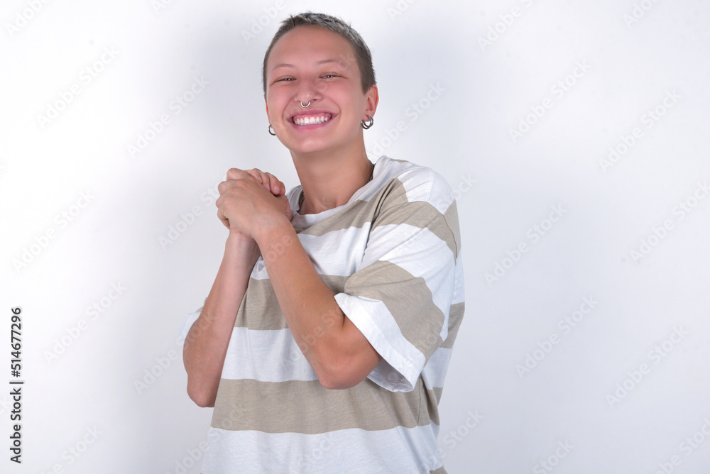 Dreamy young woman with short hair wearing striped t-shirt over white background with pleasant expression, closes eyes, keeps hands crossed near face, thinks about something pleasant Dreamy young woman with short hair wearing striped t-shirt over white background with pleasant expression, closes eyes, keeps hands crossed near face, thinks about something pleasant