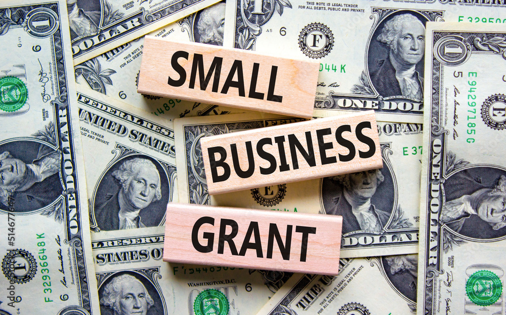 Small business grant symbol. Concept words Small business grant on wooden blocks on a beautiful background from dollar bills. Business, finacial and small business grant concept.