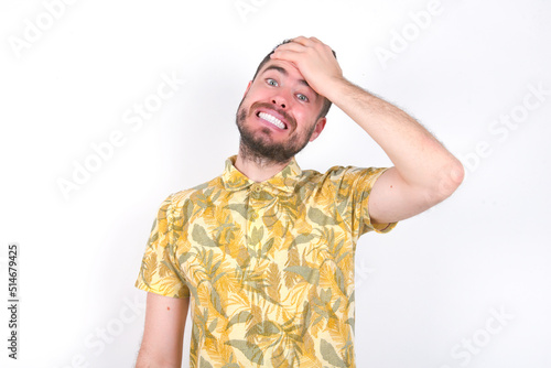 Oops, what did I do? Young caucasian man wearing Hawaiian t-shirt over white background holding hand on forehead with frightened and regret expression.