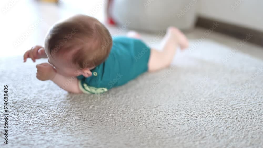 Little baby boy rolling on the floor. Cute kid opens mouth to put his fist and bangs the floor with a hand. Blurred backdrop. Little baby boy rolling on the floor. Cute kid opens mouth to put his fist and bangs the floor with a hand. Blurred backdrop.