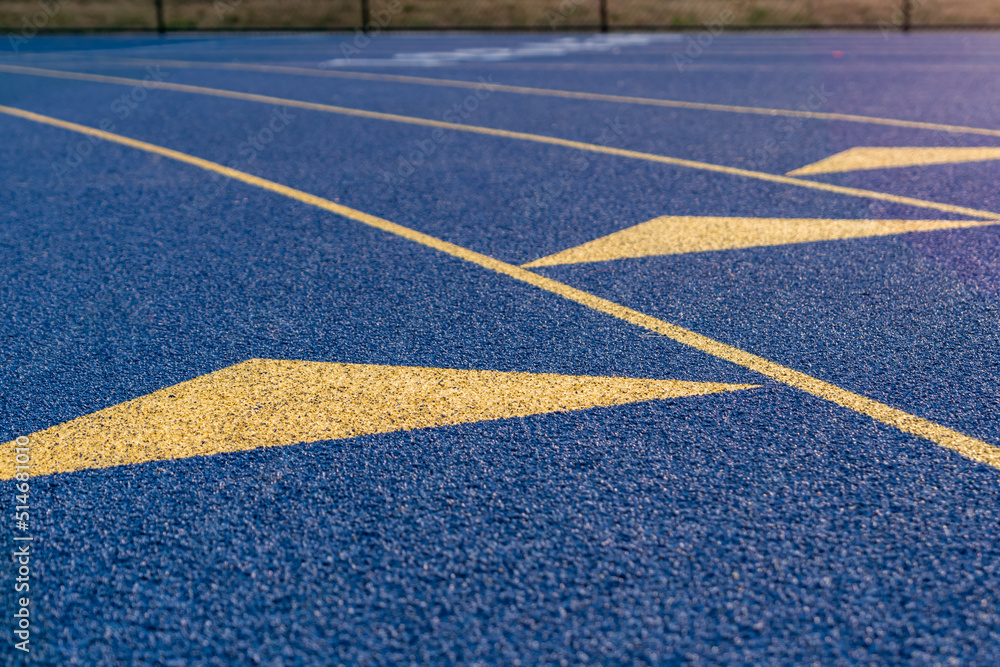 Inspiring close up of the start of an exchange zone on a new blue running track with yellow lane lines and other markings.