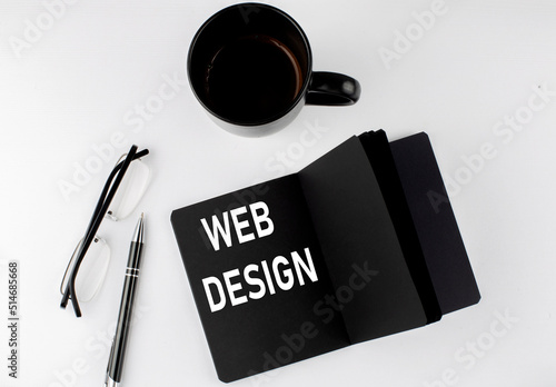 WEB DESIGN written text in small black notebook with coffee , pen and glasess on white background. Black-white style