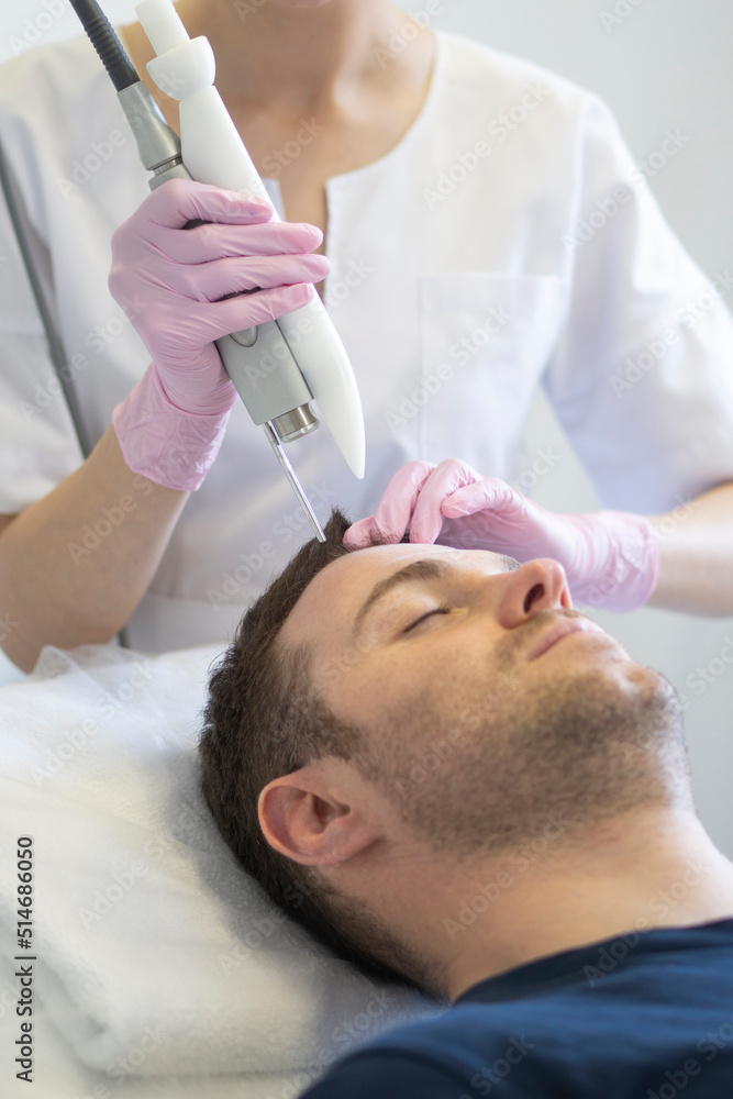 Doctor female dermatologist trichologist makes a procedure to stimulate hair growth to a patient man. Laser treatment of alopecia and hair loss Doctor female dermatologist trichologist makes a procedure to stimulate hair growth to a patient man. Laser treatment of alopecia and hair loss