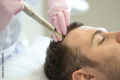 Doctor female dermatologist trichologist makes a procedure to stimulate hair growth to a patient man. Laser treatment of alopecia and hair loss .Close up