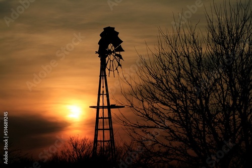 Kansas Sunset with a Windmill silhouette with trees and Sun with clouds north of Hutchinson Kansas USA out in the country. photo