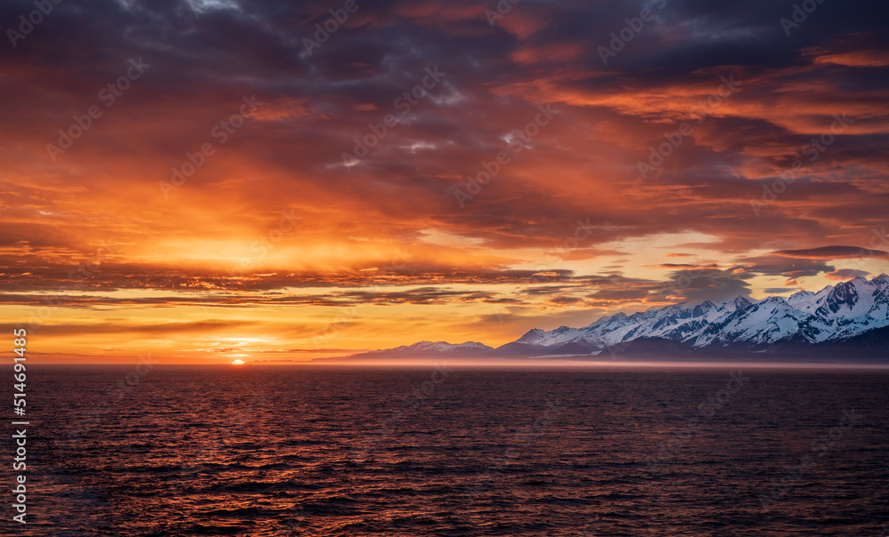 Sun on the horizon by the mountains and Mount Fairweather by Glacier Bay National Park in Alaska