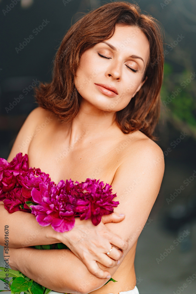 a gentle woman with closed eyes and bare shoulders and arms with a peonies.