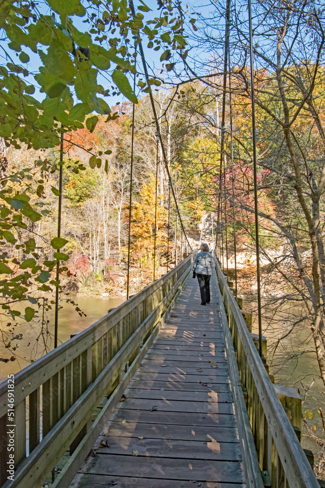 A woman crosses a suspension bridge over Sugar Creek, on an autumn day in Parke County, Indiana.