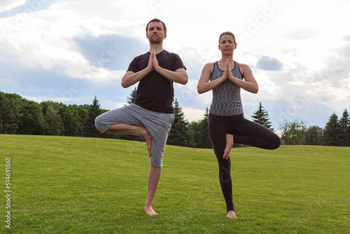 Full length view of a young couple doing the tree yoga pose together at a park