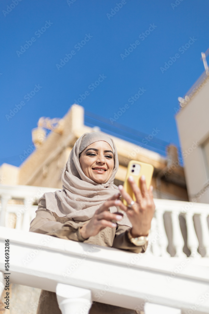 Muslim woman on the street using a phone and smiling