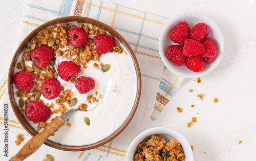 Overhead view of vanilla yogurt with granola and fresh raspberries; copy space