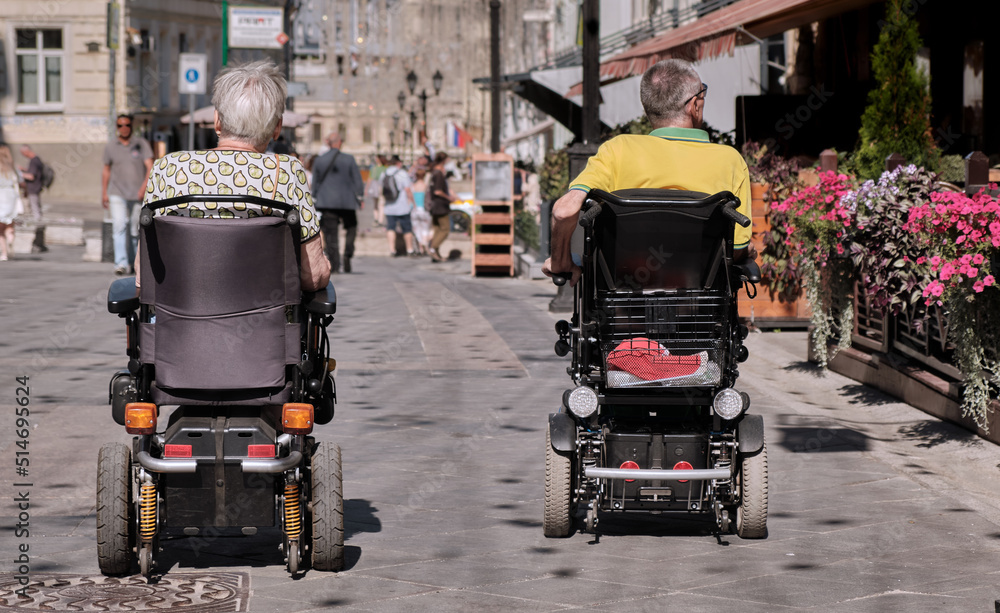 Accessible environment for people with disabilities. Happy family couple in motorized wheelchair are relaxing on city street using outdoor facilities for disabled.