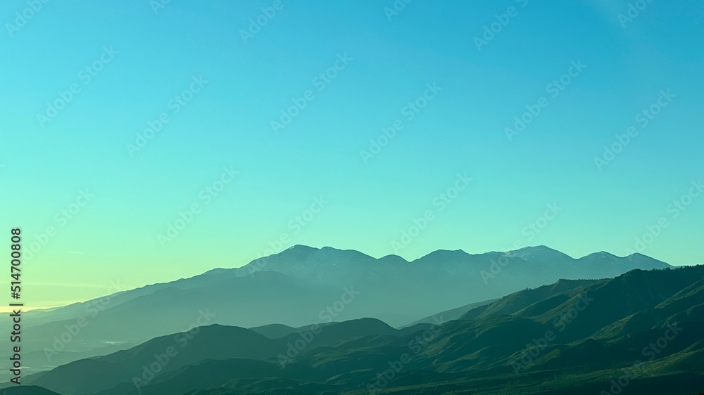 Silhouetted mountains in California, creating a flattened landscape, in shades of blue and green