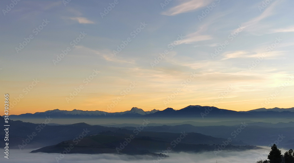Colline che galleggiano tra nebbia e nuvole mentre il sole tramonta sui monti Appennini