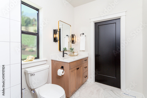 A modern farmhouse bathroom with wood cabinets  quartz countertops and black pulls.