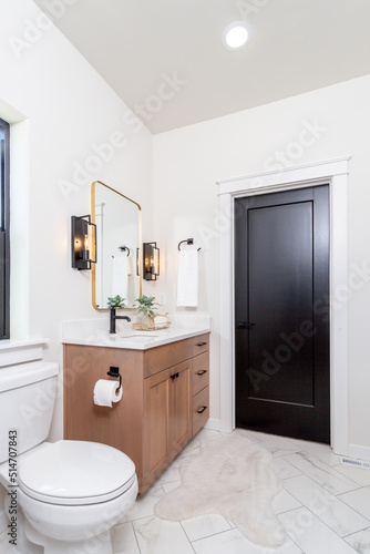 A modern farmhouse bathroom with wood cabinets  quartz countertops and black pulls.