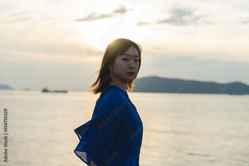夕暮れの海にいる青いワンピースの女性