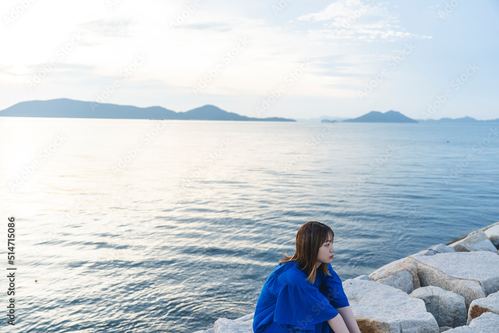 夕暮れの海にいる青いワンピースの女性