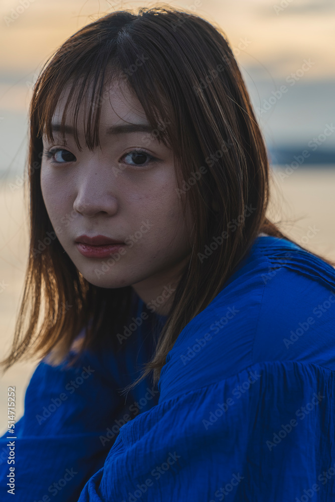 夕暮れの海にいる青いワンピースの女性