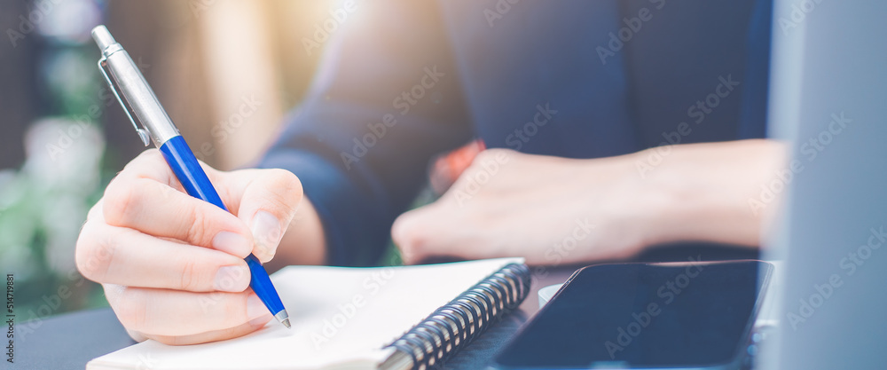 Woman hand writing on a notepad with a pen in the office.Web banner.