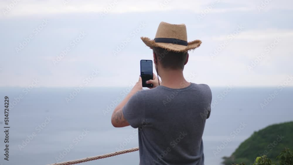 A young man in a hat astanding against the background of mountains and photographing beautiful landscapes with sea. 4k A young man in a hat astanding against the background of mountains and photographing beautiful landscapes with sea. 4k