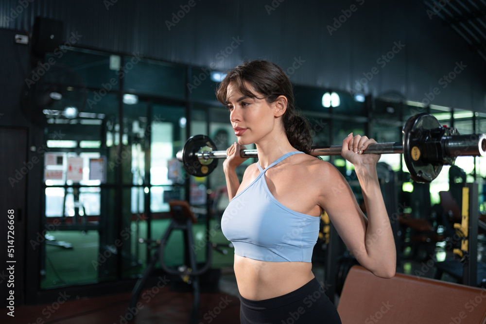 Fototapeta premium Strong fit woman in sportswear exercising with barbell for bodybuilder in fitness gym. Female workout for good health concept.