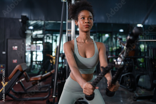 Fit young African American female athlete in sportswear exercise bodybuilder pulling down wire cable on gym equipment in fitness center.Workout for good health concept.