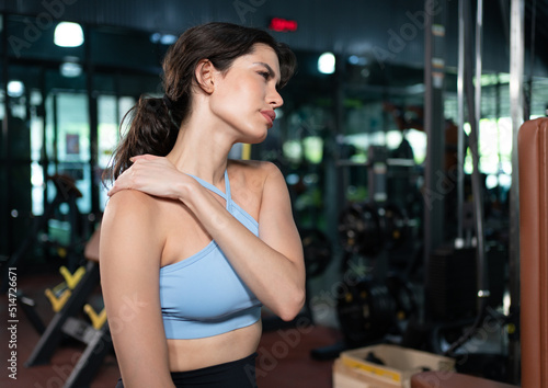 Young woman feeling pain in her shoulder muscle after fitness workout at gym