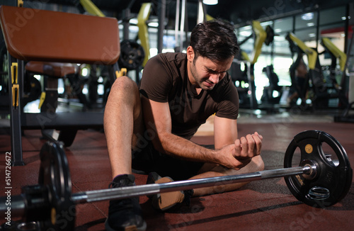 Man feeling pain in his wrist after workout lifting with barbell in fitness gym