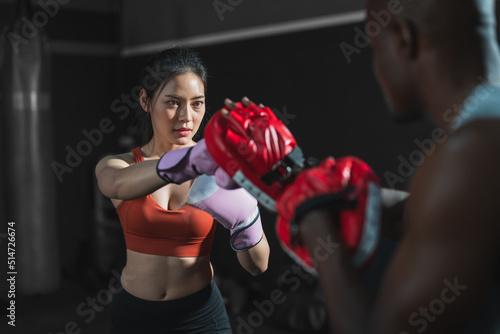 Asian fit female boxing training with her trainer at gym.Sportwoman  wearing boxing gloves exercise and punch to pads for boxing © Supachai