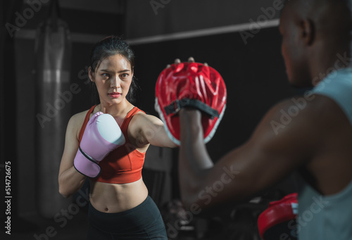 Asian fit female boxing training with her trainer at gym.Sportwoman wearing boxing gloves exercise and punch to pads for boxing