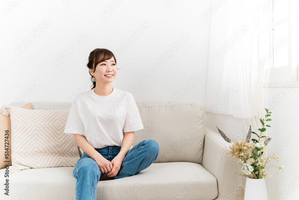 家のソファに座る笑顔の日本人女性（窓・紫外線）
