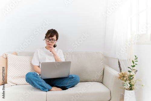家のソファでパソコンを使うデニム姿の日本人女性（困る・悩む） 
