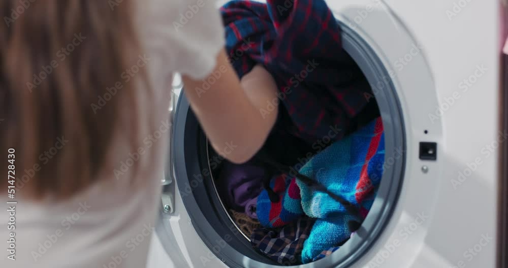 Close up shot of the drum. A little girl puts colorful clothes in the wash. The child helps mother with the housework, closes the washing machine door. Close up shot of the drum. A little girl puts colorful clothes in the wash. The child helps mother with the housework, closes the washing machine door.