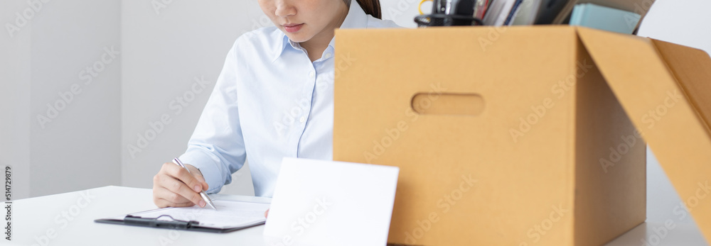 Businesswoman in a blue shirt sat filling out the letter of resignation and there was a box of personal work equipment next to it, Prepare to move to a new place of work or be laid off, been dismissed Businesswoman in a blue shirt sat filling out the letter of resignation and there was a box of personal work equipment next to it, Prepare to move to a new place of work or be laid off, been dismissed